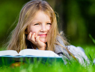 Pretty little girl reads interesting book lying on the grass 