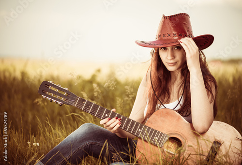 Obrazy Country & Western  mloda-stylowa-kowbojka-z-gitara-na-wiosennej-lace