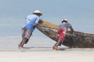 Zwei Fischer schieben ein Boot am Strand von Beau Vallon