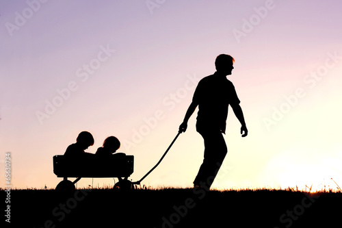 Fotografija  Silhouette of Father Pulling Sons in Wagon at Sunset
