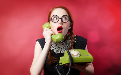 Wall Mural - Redhead girl with green phone on red background.