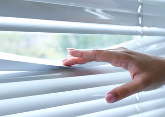 Female hand separating slats of venetian blinds with a finger