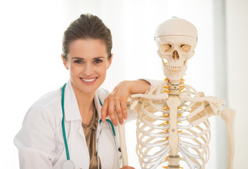 Portrait of smiling medical doctor woman near human skeleton 