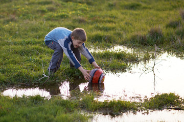 boy gets ball with puddles in the grass