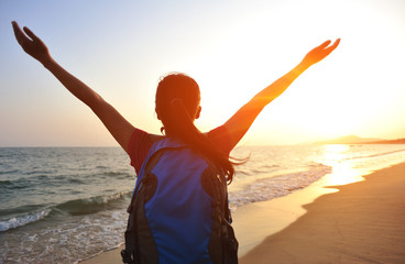 Wall Mural - cheering woman hiker open arms at sunrise seaside beach  open be