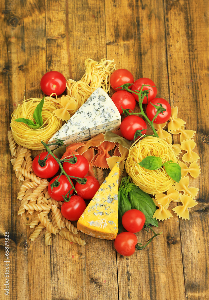 Different pasta, cheese and tomatoes on wooden table close-up