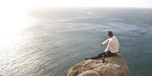 Young Handsome Guy Sitting On Rock Above Ocean