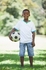 Poster - Little boy holding football in the park smiling at camera