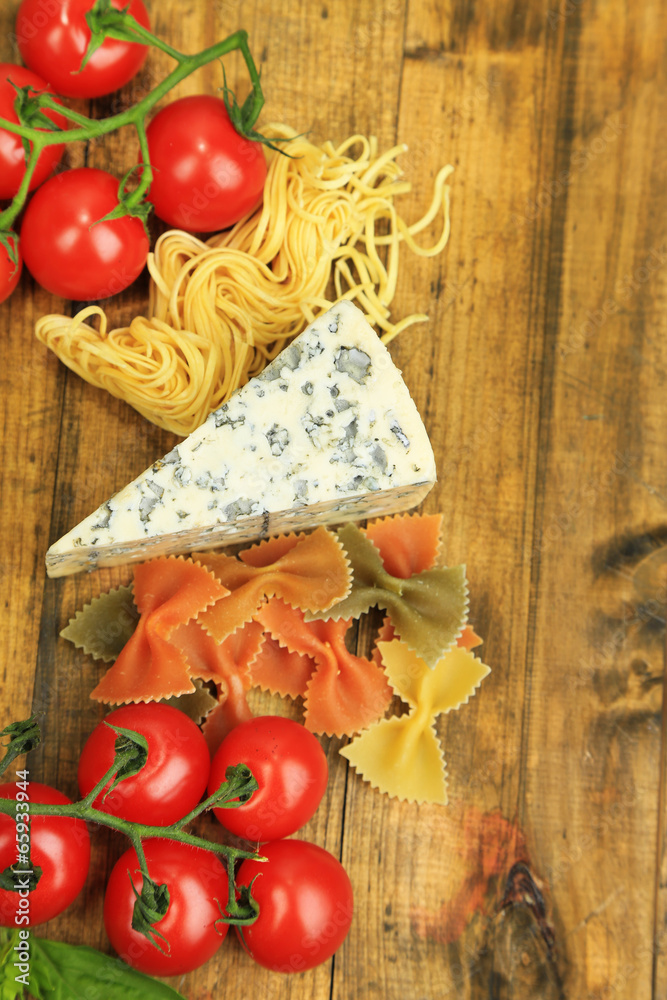 Different pasta, cheese and tomatoes on wooden table close-up