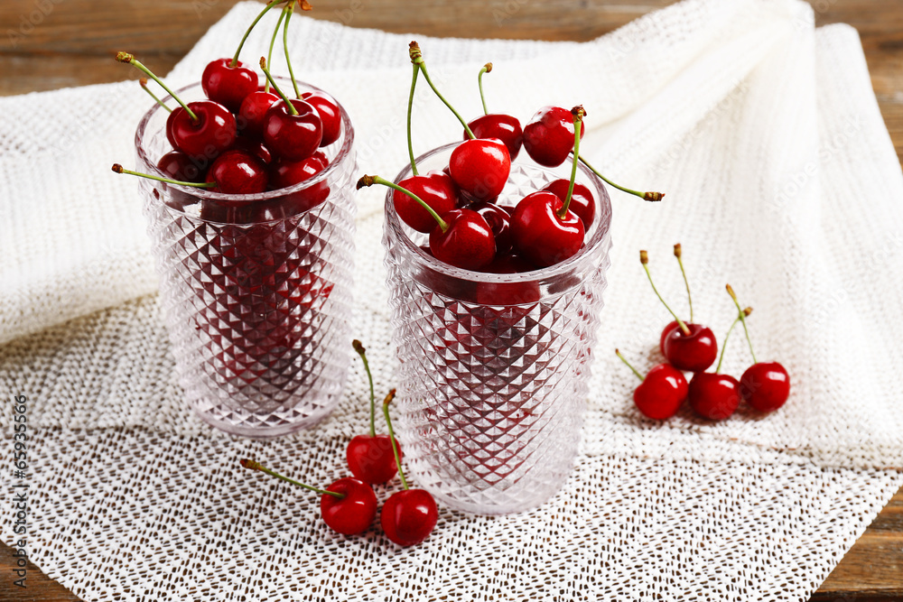 Sweet cherries in glasses on wooden table