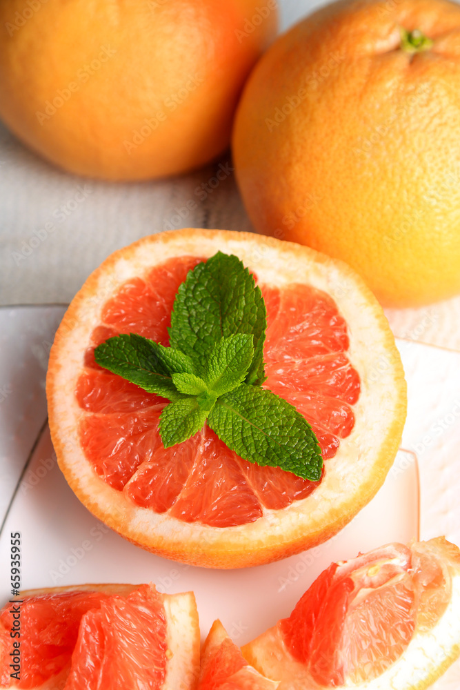 Ripe grapefruits on plate on color wooden background