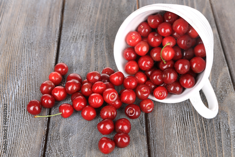 Sweet cherries in mug on wooden background