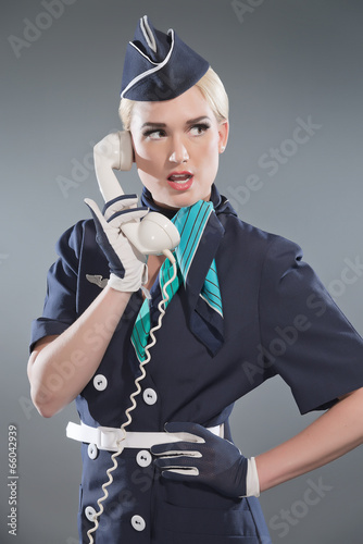 Naklejka dekoracyjna Calling retro blonde stewardess wearing blue suit. Holding white