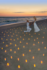 Fototapete - couple at sea beach in candles against sunset