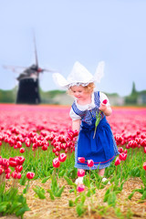 Little girl in a national Dutch costume in tulips field with win