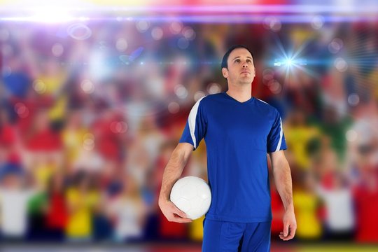 Composite image of handsome football player holding the ball