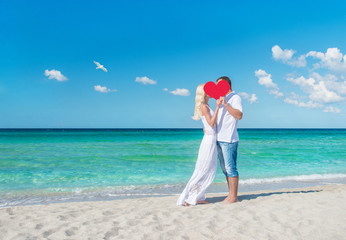 Fototapete - Loving couple at sunny sea beach with red heart