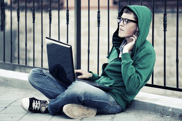 Young man with laptop sitting on the sidewalk