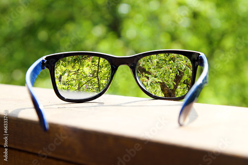 Fényképezés eyeglasses in the hand over blurred tree background