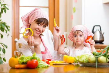 Wall Mural - kid girl and her mother cooking in kitchen at home