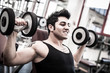 © pio3 - Young man exercising with dumbbells in a gym. Filtered image.