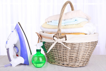 Colorful towels in basket, iron on light background