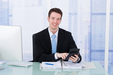 Poster - Confident Businessman Using Calculator At Office Desk