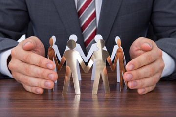 Wall Mural - Businessman Protecting Team Of Paper People On Desk