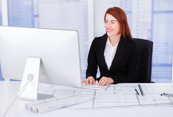 Poster - Businesswoman Using Computer With Blueprints At Desk