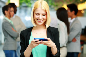 Wall Mural - Happy businesswoman using smartphone in front of colleagues