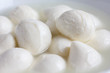 Small white mozzarella balls in a white dish with liquid.