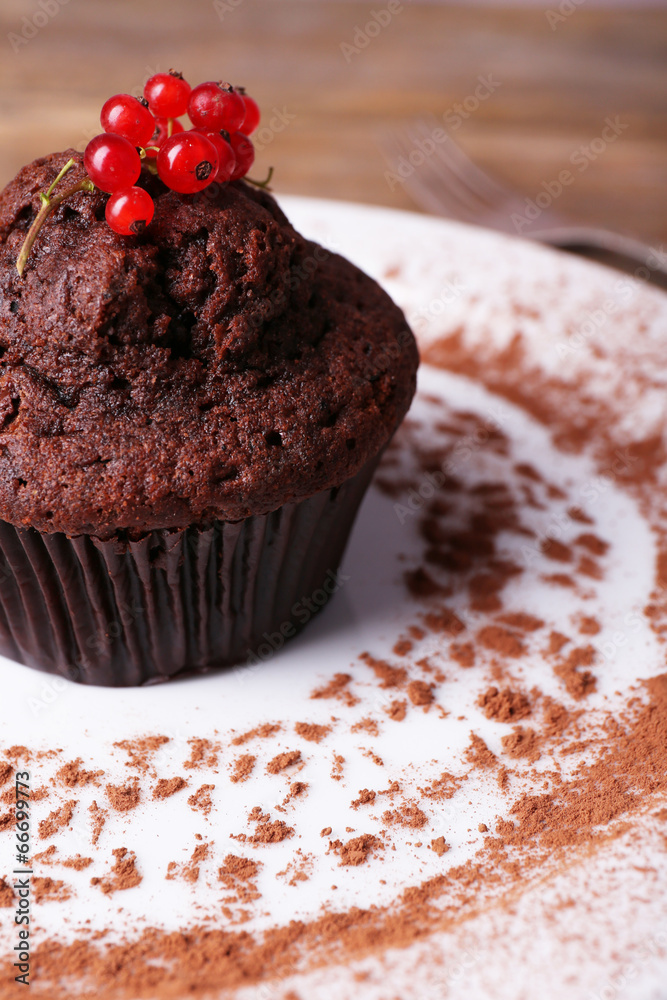 Chocolate muffin with red currant on plate on wooden background