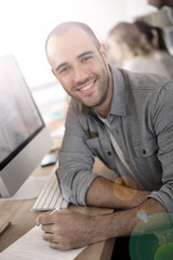 Wall Mural - Cheerful guy sitting in front of desktop computer