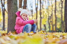 Little Girl Sits Leaning At Tree Trunk And Looking