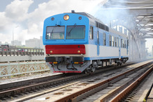 Small Blue Train Rides Rails On Railway Bridge At Summer Day.