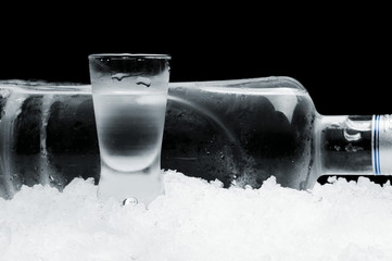 Bottle with glass of vodka lying on ice on black background