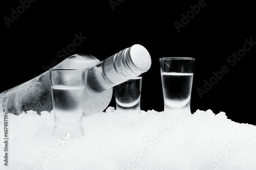 Fotomural Bottle with glasses of vodka lying on ice on black background