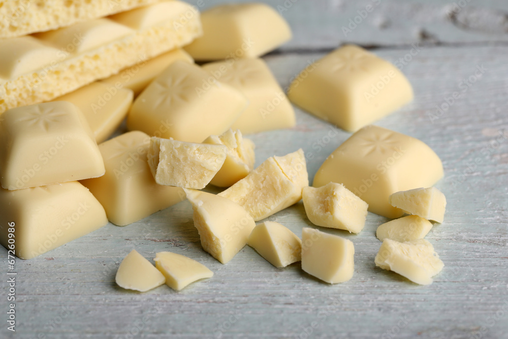 Broken white chocolate bar on color wooden background