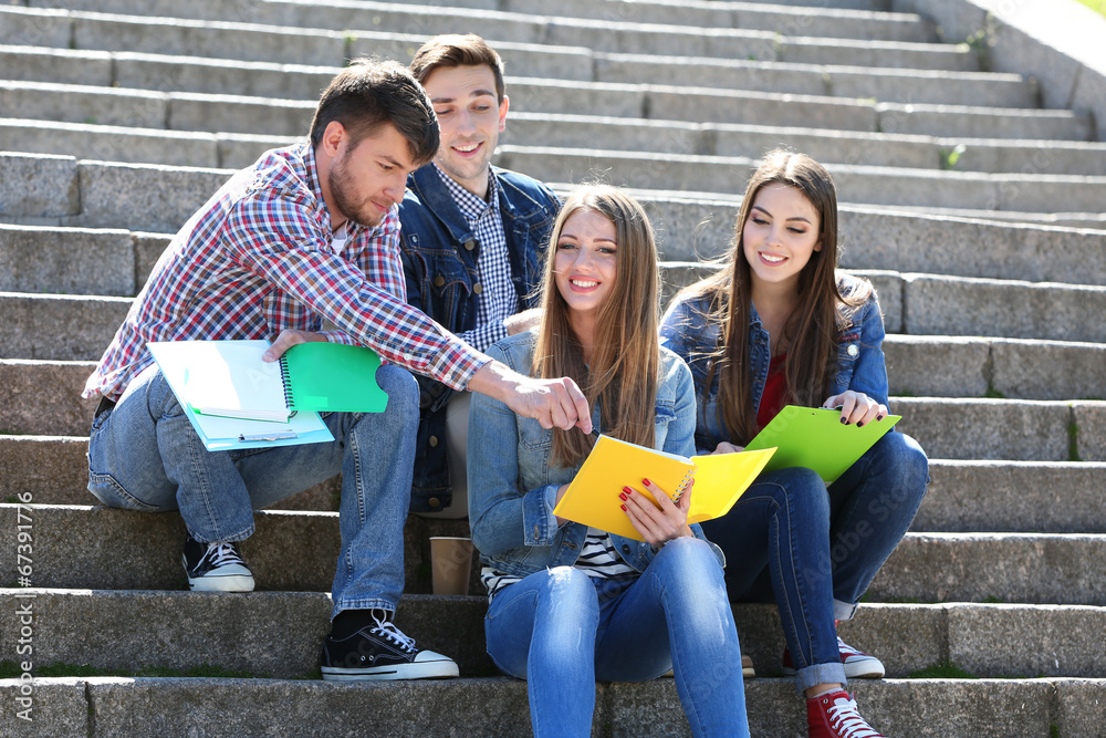 Happy students sitting on stairs in park