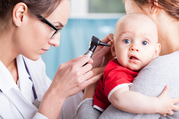 Wall Mural - Doctor examining baby boy with otoscope