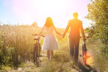 Young happy bride and groom carry bikes in the field