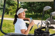 Young Cheerful Woman With Bottle Of Water Driving Golf Cart