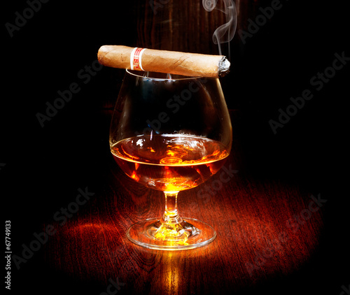 Naklejka dekoracyjna Cognac and cigar. Glass of brandy over dark background