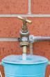 Outside tap on brick wall filling a blue bucket