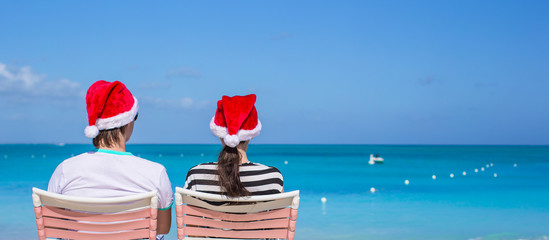 Wall Mural - Back view of young couple in Santa hats enjoy beach vacation