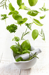 green herbs falling into mortar and pestle