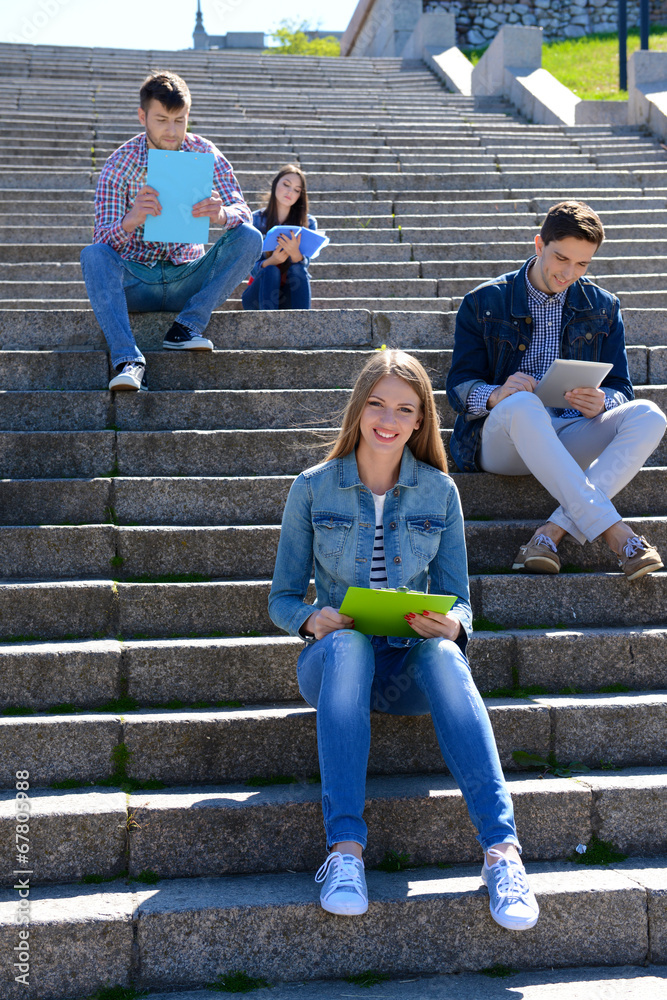 Happy students sitting on stairs in park