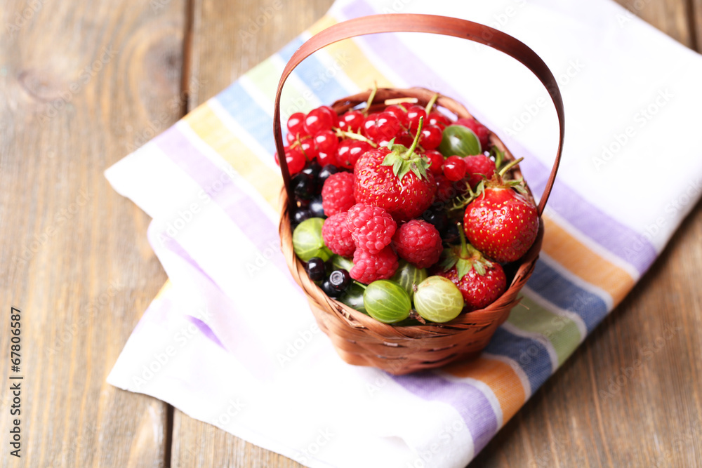 Forest berries in wicker basket, on wooden background
