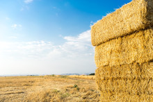 Piled Hay Bales On A Field Against Blue Sky With Clouds.