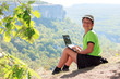 Smiling boy in green t-shirt with a netbook on top of the mounta